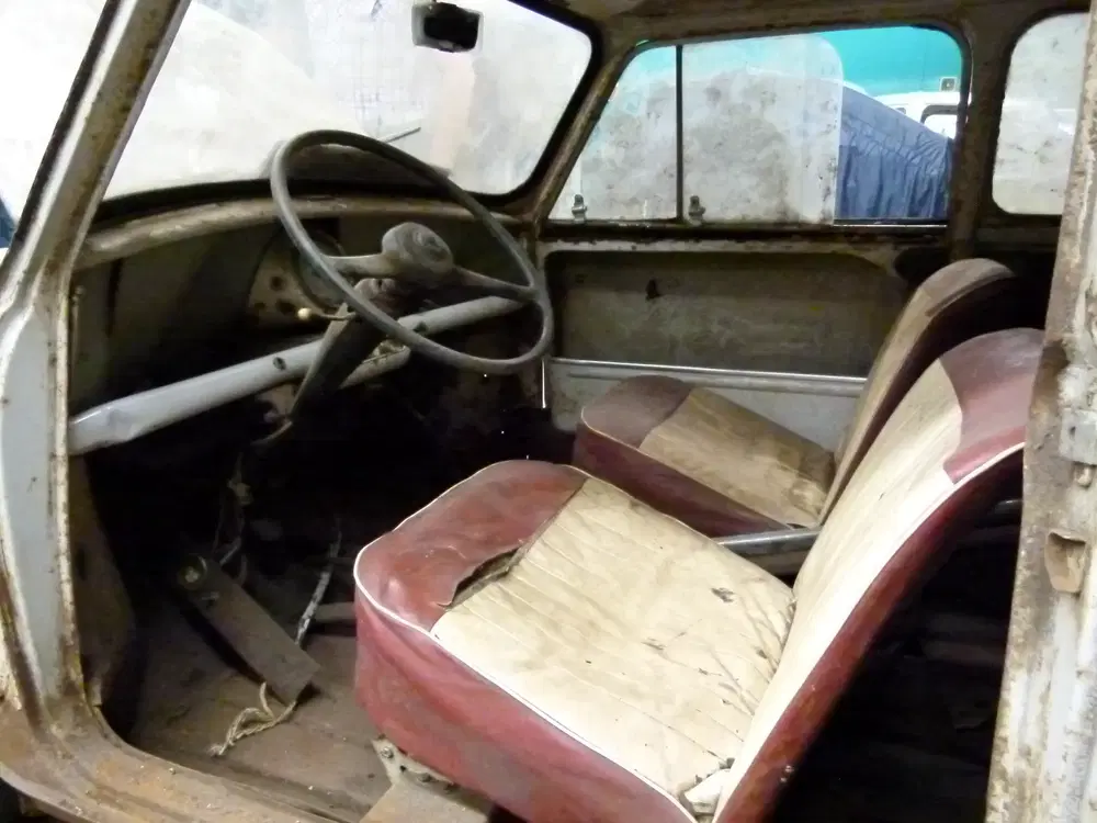 Intérieur d'une Citroën 2CV ancienne avec sièges usés et volant rétro.