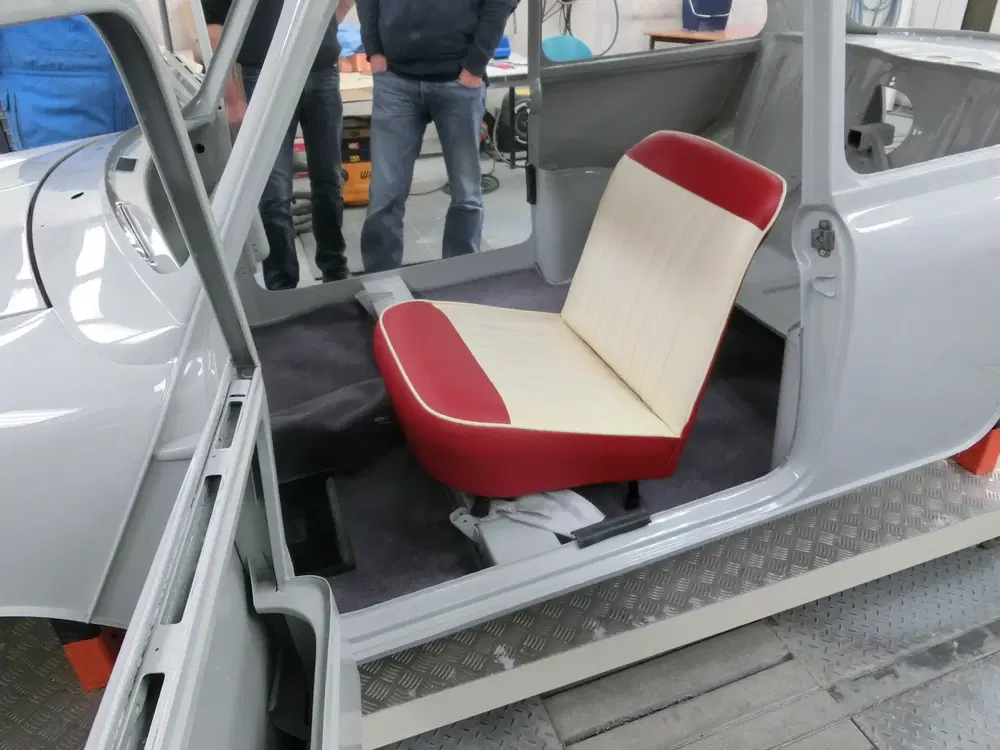 Restauration d'une voiture ancienne avec intérieur rouge et blanc, siège avant installé.